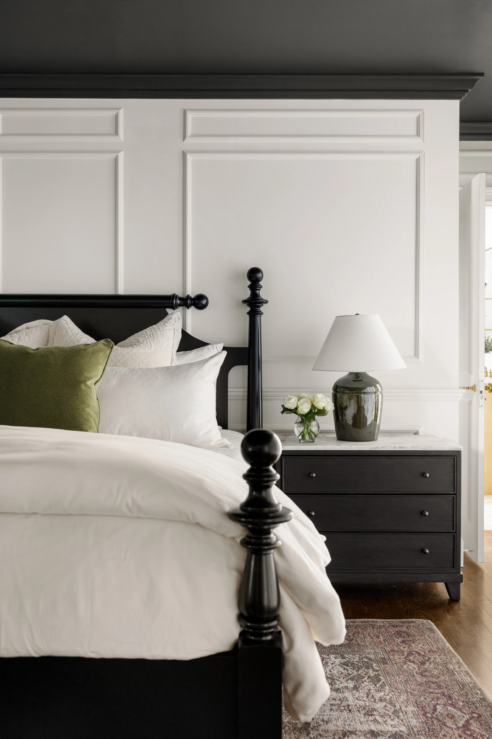 Primary bedroom with black four-poster bed, picture-frame molding and green pillow at Project Five Fourteen in Providence, Rhode Island