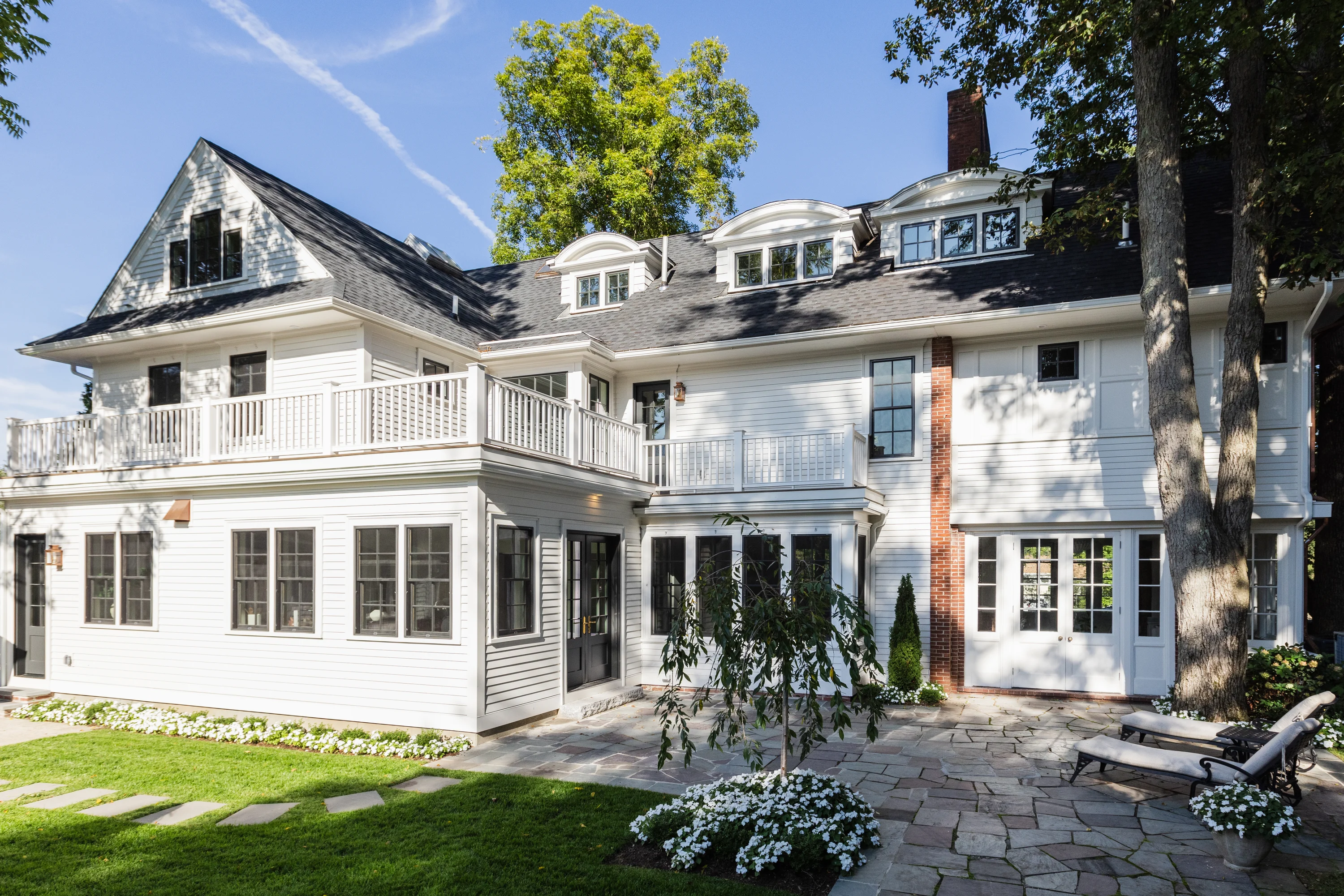 White shingle coastal home exterior with stone patio and dormers in Rhode Island