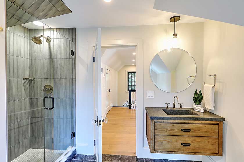 Guest bathroom renovation featuring a warm wood vanity and round mirror.