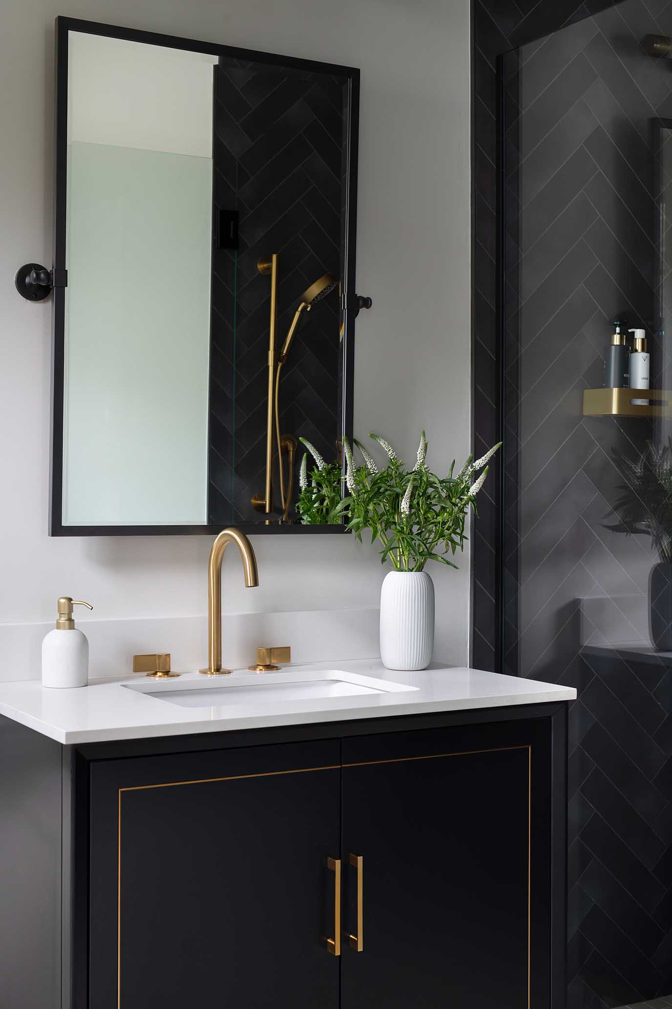 A sophisticated bathroom design featuring a black custom vanity, gold fixtures, and a herringbone tiled shower, representing Hill & Harbor's integrated services.